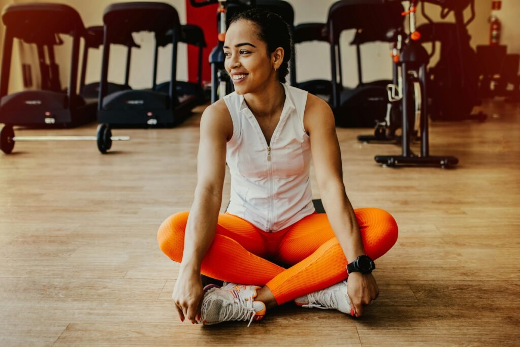 Confident woman in bright workout attire smiling while sitting in a gym.